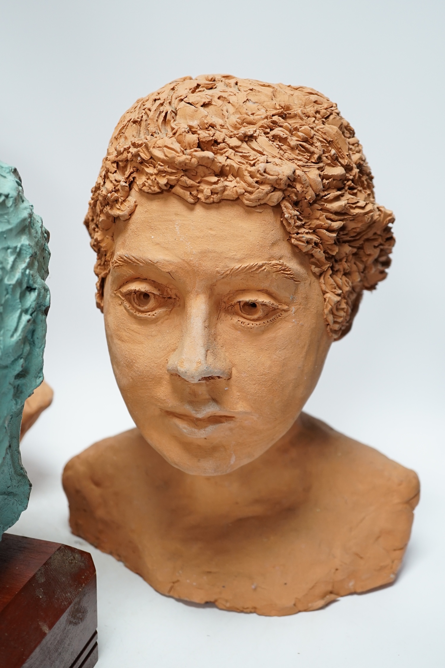 Four art pottery sculpted heads on stands, two terracotta and two painted verdigris green, largest 34cm high